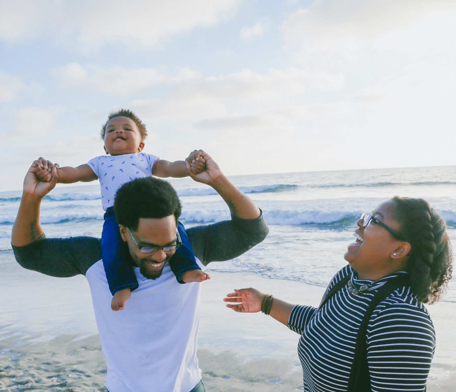 Família feliz na praia erguendo o bebê